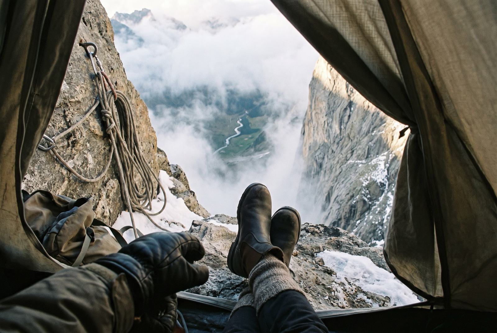 Boots crossed at the edge of a tent platform, and beyond, a thousand metres of air above cloud and a distant valley floor.